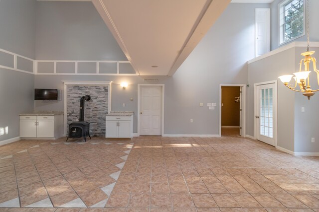 unfurnished living room featuring a high ceiling, a notable chandelier, a wood stove, and light tile patterned floors