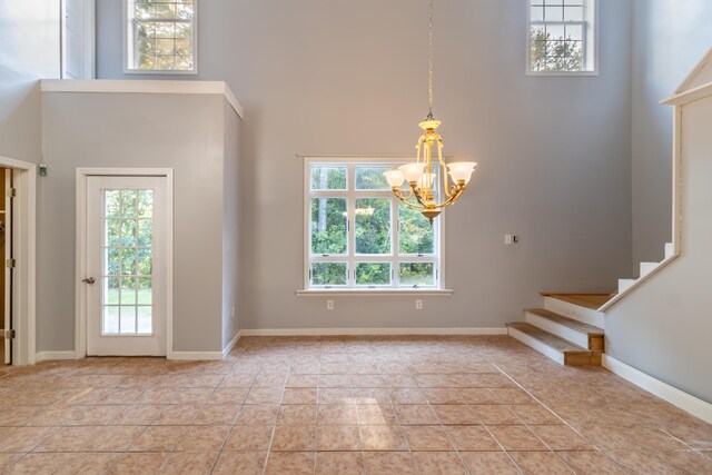 foyer entrance featuring a wealth of natural light, an inviting chandelier, a towering ceiling, and light tile patterned floors