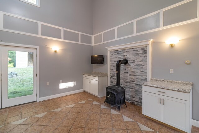 unfurnished living room featuring a towering ceiling, a wood stove, and light tile patterned flooring