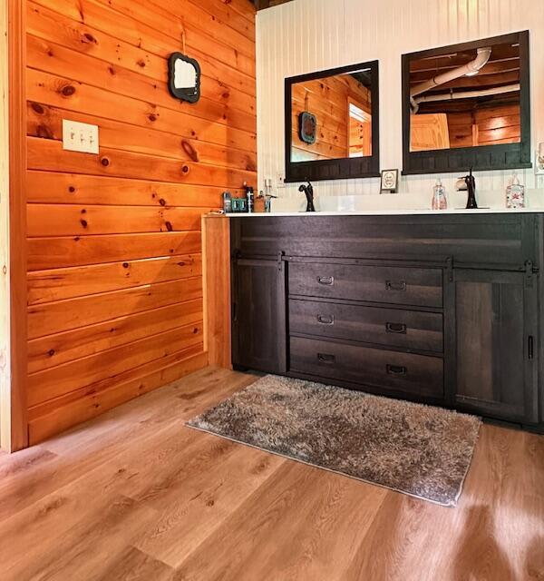 bar featuring light wood-type flooring, a sink, and wooden walls