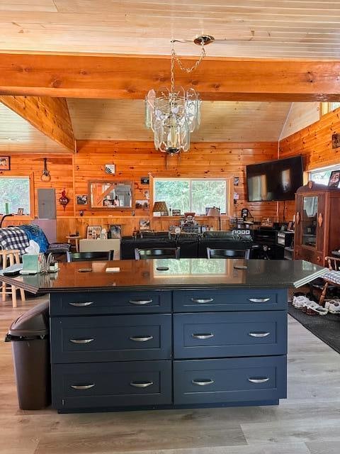 kitchen with a kitchen island with sink, lofted ceiling with beams, wood walls, and light wood-type flooring