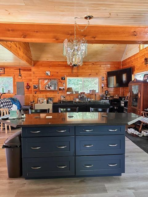 kitchen with light wood finished floors, wooden walls, a center island, vaulted ceiling with beams, and an inviting chandelier