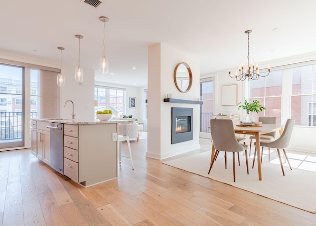 kitchen with hanging light fixtures, light hardwood / wood-style floors, sink, a center island with sink, and stainless steel dishwasher