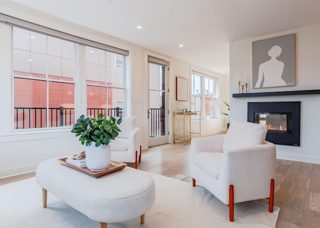 living area featuring recessed lighting, baseboards, a glass covered fireplace, and light wood finished floors