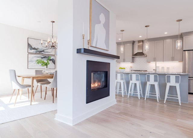 kitchen with decorative backsplash, gray cabinets, a breakfast bar area, and wall chimney range hood