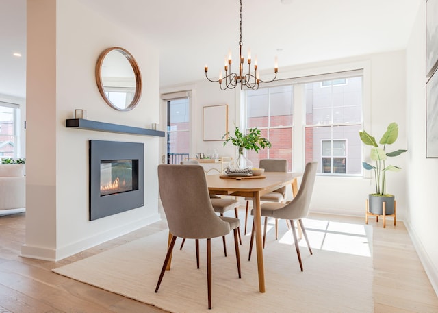 dining space with a glass covered fireplace, an inviting chandelier, baseboards, and light wood-type flooring