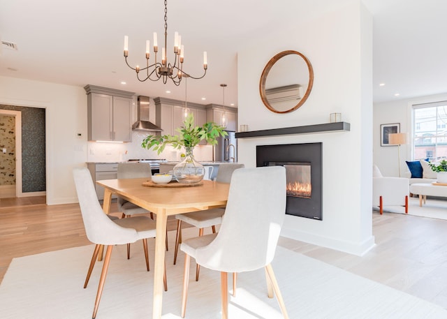 dining room featuring baseboards, a glass covered fireplace, recessed lighting, light wood-style floors, and a notable chandelier