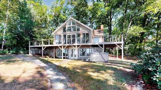 rear view of house featuring a wooden deck, a yard, and a hot tub