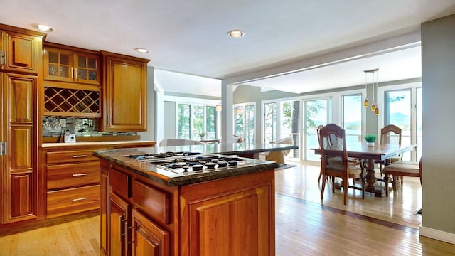 kitchen with hanging light fixtures, light hardwood / wood-style floors, stainless steel gas stovetop, decorative backsplash, and a kitchen island