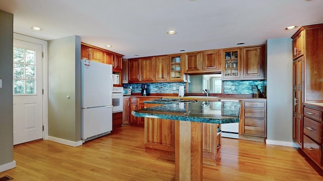 kitchen with white appliances, dark stone counters, light wood-type flooring, a kitchen island, and a breakfast bar area