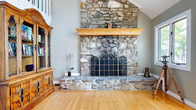 living room featuring a stone fireplace, wood-type flooring, and vaulted ceiling