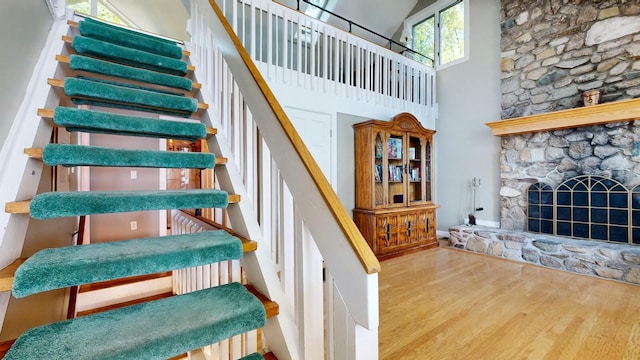 staircase featuring wood-type flooring, a fireplace, and high vaulted ceiling