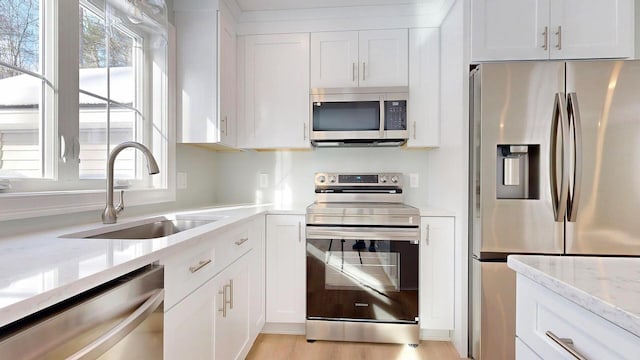 kitchen featuring sink, white cabinetry, stainless steel appliances, light stone countertops, and a healthy amount of sunlight