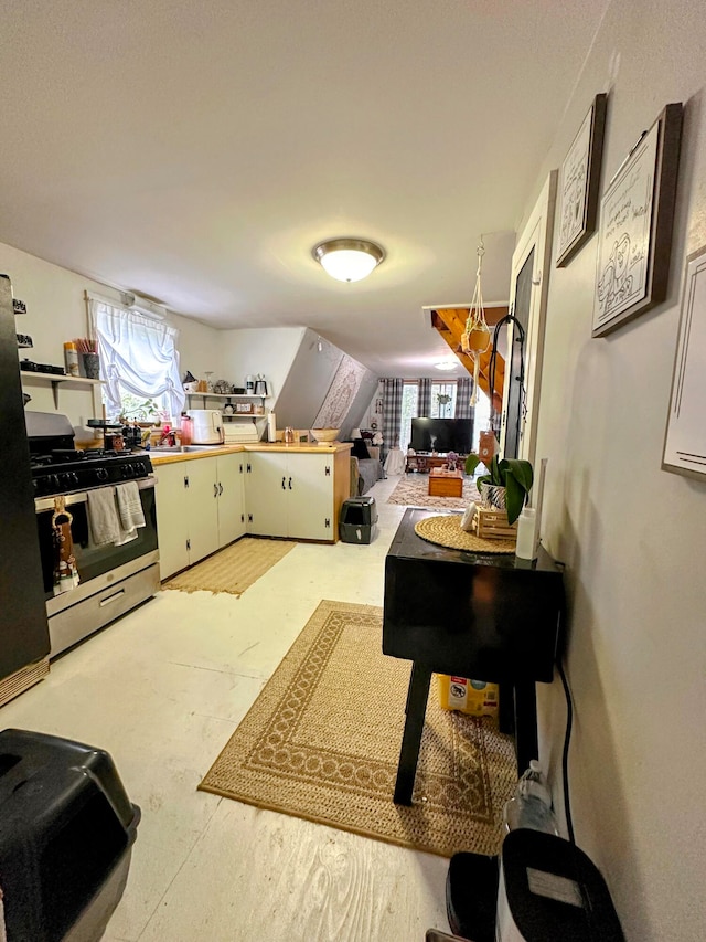 kitchen with white cabinets, stainless steel gas stove, kitchen peninsula, and a wealth of natural light