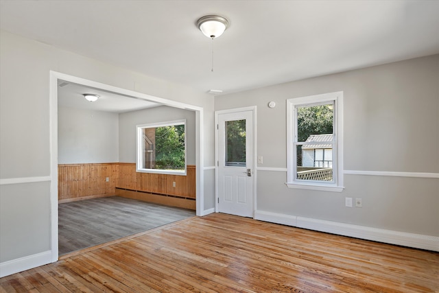 foyer entrance featuring a baseboard heating unit, a wealth of natural light, wood walls, and light hardwood / wood-style floors