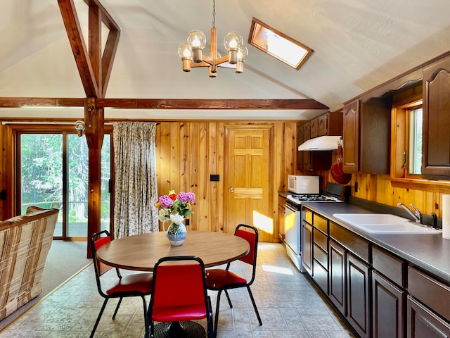 carpeted dining room with a notable chandelier, wooden walls, lofted ceiling with skylight, and sink