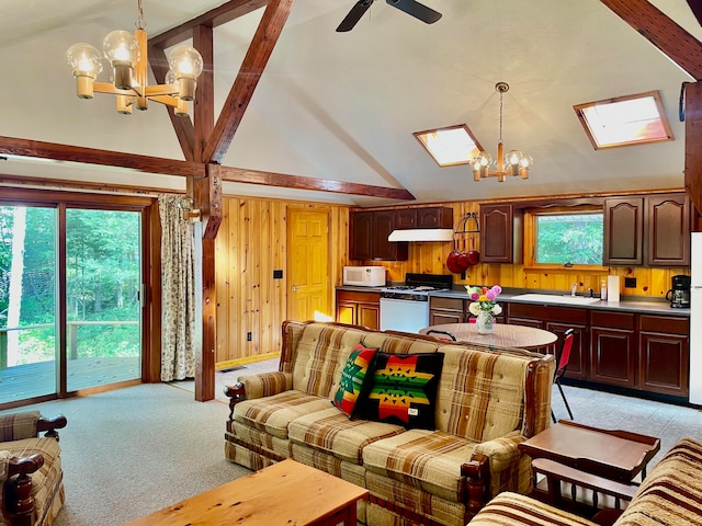 carpeted living room with sink, ceiling fan with notable chandelier, high vaulted ceiling, wooden walls, and a skylight