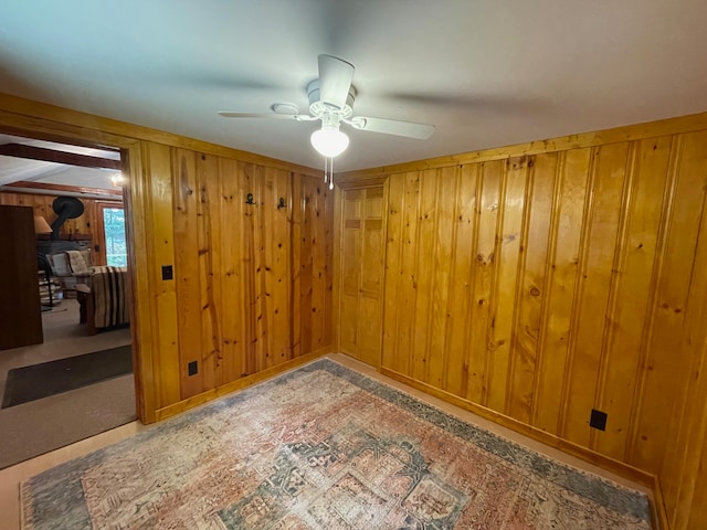 unfurnished room featuring a wood stove, wood walls, and ceiling fan