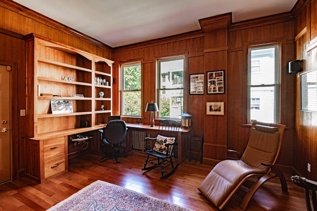 office featuring dark wood-type flooring, built in desk, wood walls, and a wealth of natural light