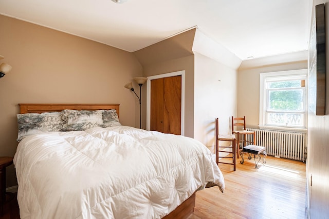 bedroom featuring a closet, radiator heating unit, wood-type flooring, and vaulted ceiling