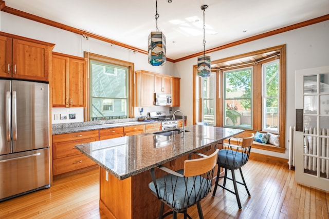 kitchen with ornamental molding, appliances with stainless steel finishes, decorative light fixtures, and a kitchen island with sink