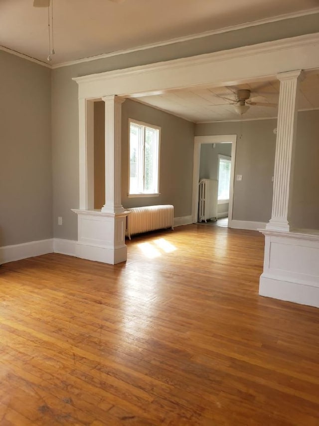 spare room featuring ceiling fan, radiator, decorative columns, and wood-type flooring