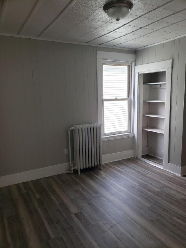 unfurnished bedroom featuring dark hardwood / wood-style flooring, radiator heating unit, and a closet