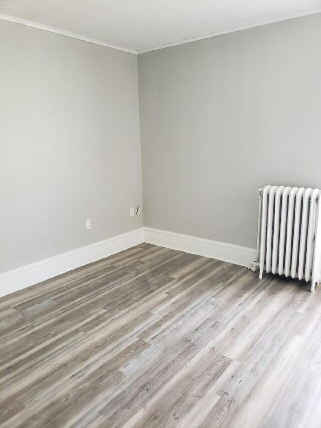 unfurnished room featuring light hardwood / wood-style flooring, ornamental molding, and radiator heating unit