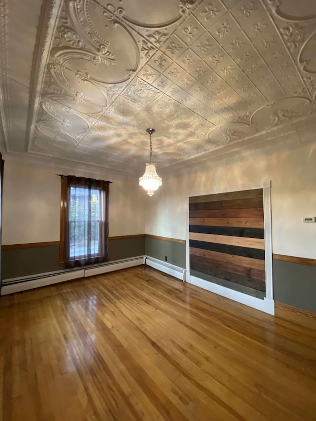 interior space featuring an inviting chandelier, wood-type flooring, an ornate ceiling, a wainscoted wall, and a baseboard radiator