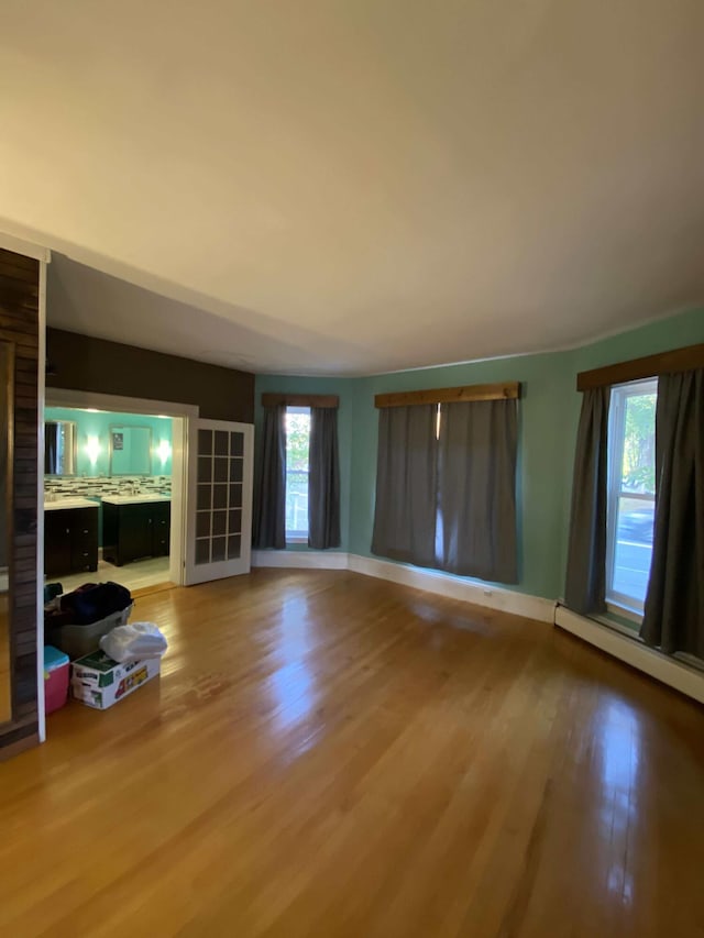 unfurnished living room with baseboards, baseboard heating, and light wood finished floors