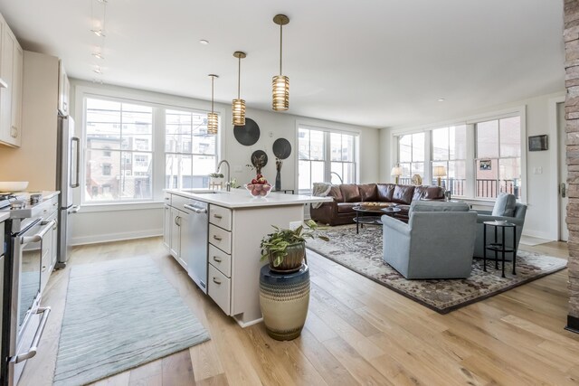 kitchen with a kitchen island with sink, white cabinetry, pendant lighting, and a healthy amount of sunlight