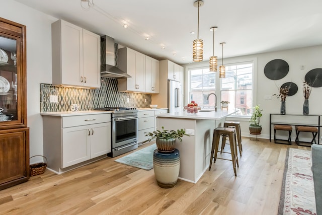 kitchen featuring an island with sink, white cabinets, pendant lighting, stainless steel appliances, and wall chimney range hood