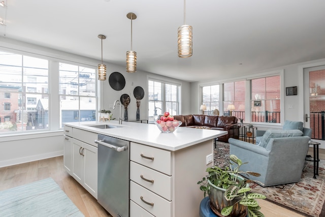 kitchen featuring hanging light fixtures, white cabinets, light hardwood / wood-style flooring, stainless steel dishwasher, and a kitchen island with sink