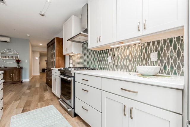 kitchen featuring stainless steel gas range, white cabinetry, wall chimney range hood, and light wood-type flooring