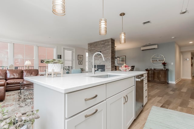 kitchen featuring white cabinets, pendant lighting, light wood-type flooring, a kitchen island with sink, and sink