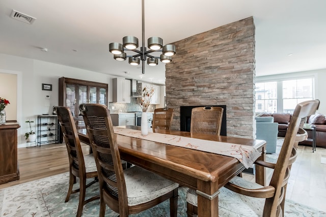 dining room with a notable chandelier, a fireplace, and light wood-type flooring