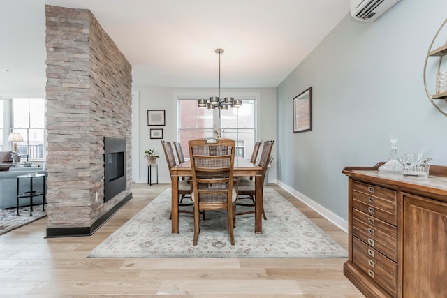 dining area with a notable chandelier, light wood-type flooring, a fireplace, and a healthy amount of sunlight