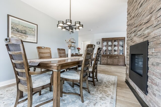 dining area with a stone fireplace, an inviting chandelier, and light hardwood / wood-style flooring