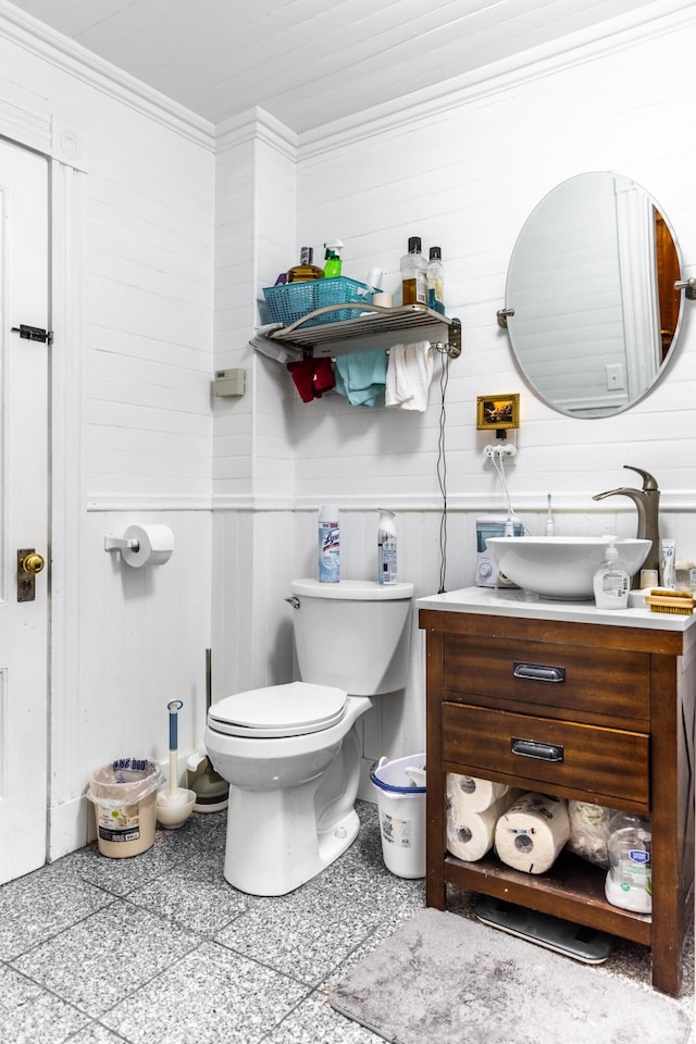 bathroom with toilet, ornamental molding, vanity, and wood walls