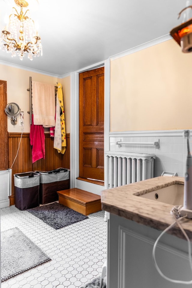 mudroom with radiator, a wainscoted wall, an inviting chandelier, ornamental molding, and a sink