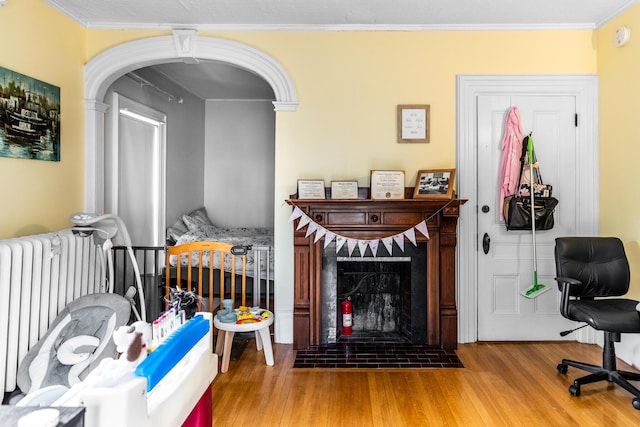 living room featuring a fireplace with flush hearth, wood finished floors, crown molding, and radiator heating unit