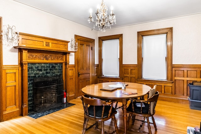 dining area featuring ornamental molding, light hardwood / wood-style flooring, a tiled fireplace, and an inviting chandelier