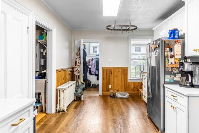 kitchen with wooden walls, radiator, stainless steel refrigerator, light wood-type flooring, and white cabinets