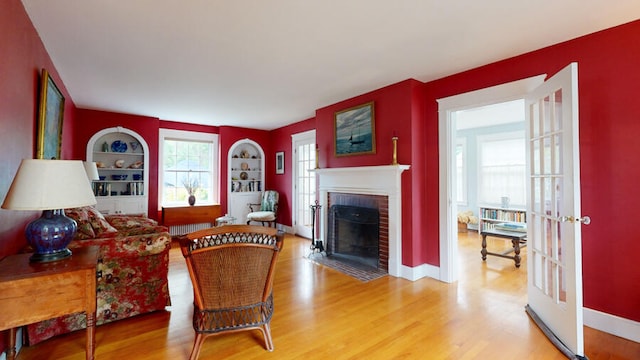 living room featuring a brick fireplace, built in shelves, and wood-type flooring