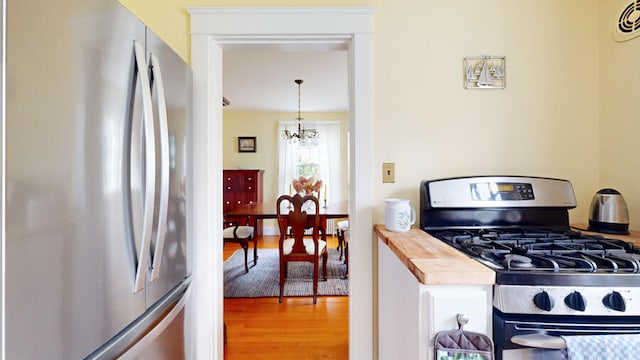 kitchen with pendant lighting, stainless steel appliances, wooden counters, light wood-type flooring, and an inviting chandelier