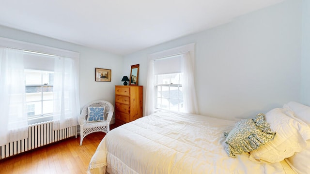 bedroom featuring radiator heating unit, wood-type flooring, and multiple windows