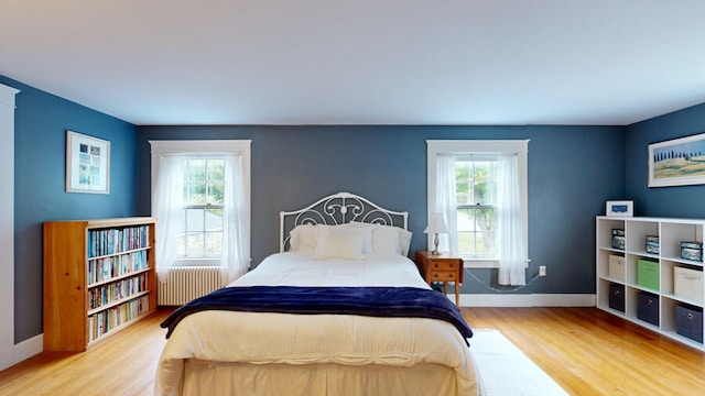 bedroom with radiator heating unit, wood-type flooring, and multiple windows