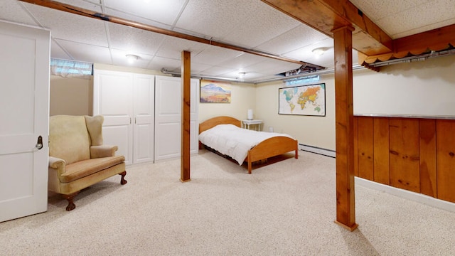 bedroom with carpet floors, a paneled ceiling, wood walls, and a baseboard heating unit