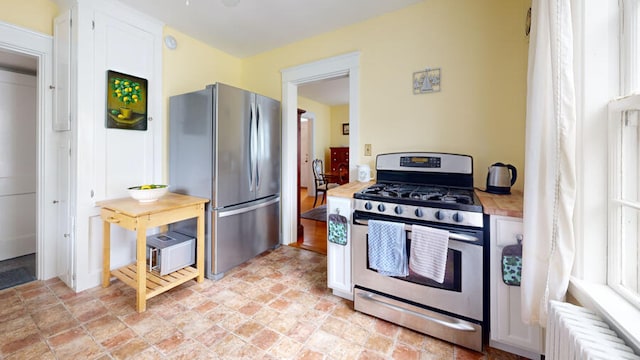 kitchen featuring appliances with stainless steel finishes, radiator, wooden counters, and white cabinetry