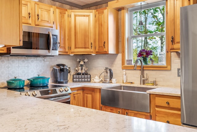 kitchen with light stone countertops, appliances with stainless steel finishes, sink, and decorative backsplash